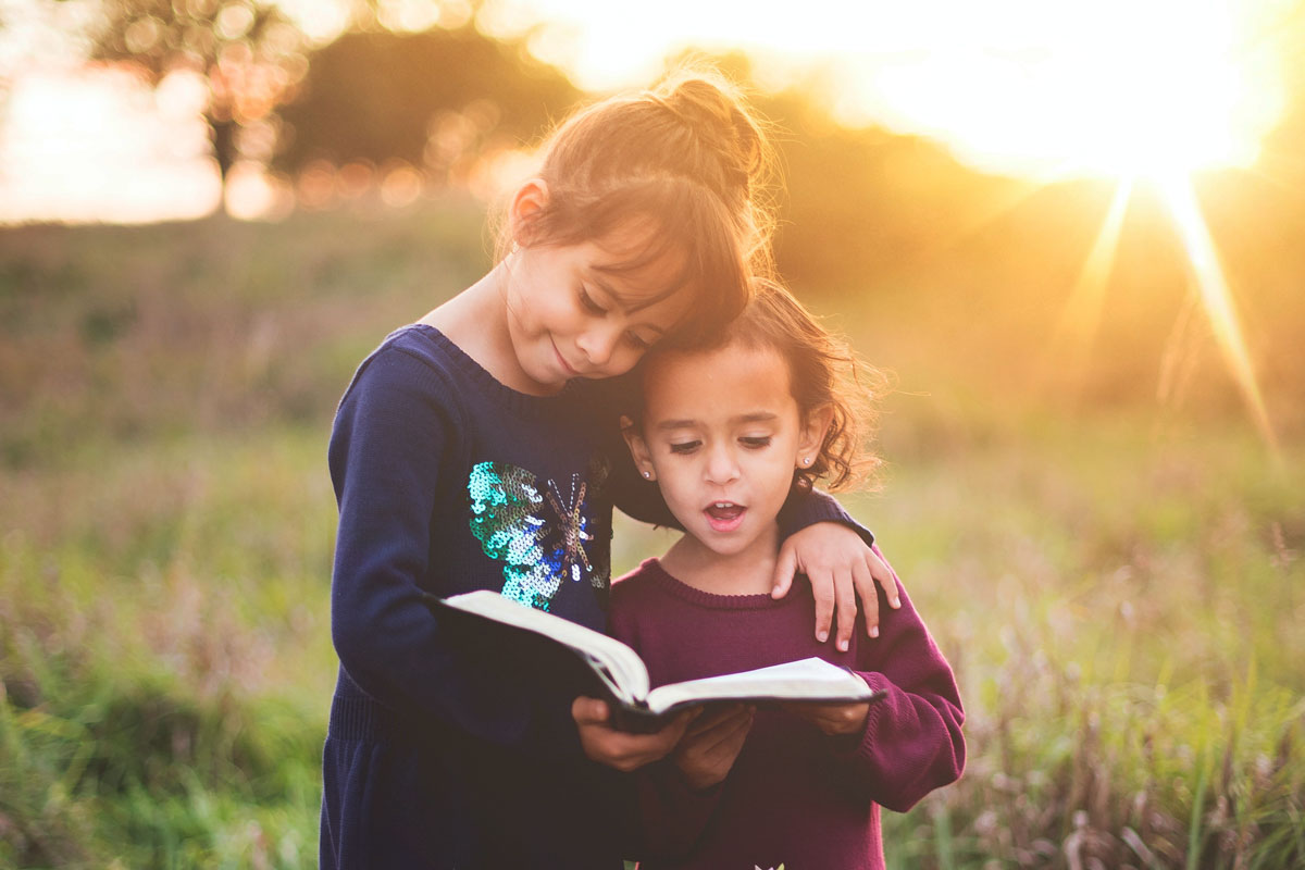 Two kids reading a book in a field